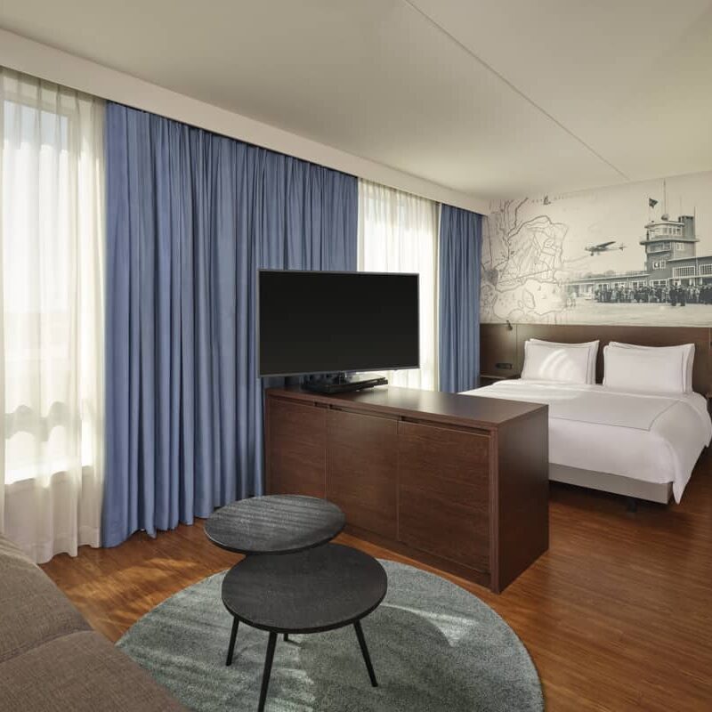 Grote kamer met een queen-size bed, een tv-meubel van donker hout, twee zwarte salontafels en een klein deel van een slaapbank