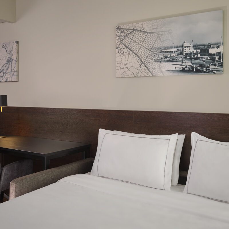 Close-up van een queen-size bed met een hoofdbord van donker hout en een bureau met een fluwelen stoel