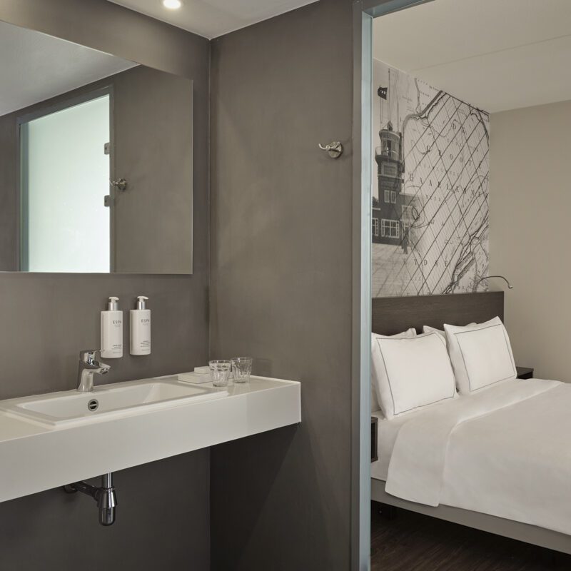 Half image of wheelchair accessible bathroom with sink and ESPA amenities and half image of queen bed